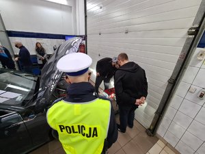 Pracownik i właścicel sprawdzają oświetlenie w pojeździe przygląda się policjant