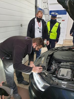 Mechanik sprawdza światła w pojeździe a przygląda się właściciel i policjant