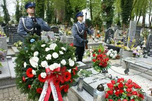 zdjęcie zrobione na cmentarzu na pierwszym planie wiązanki kwiatów i nagrobki w tle stoją policjanci z kompanii honorowej