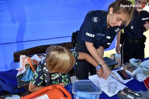 Na zdjęciu widać jak policjantka  odciska linie papilarne dziecku na kartce papieru.