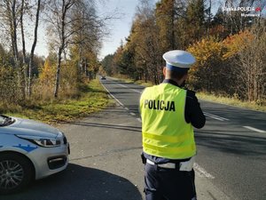 Na zdjęciu widzimy umundurowanego funkcjonariusza wydziału ruchu drogowego dokonującego pomiaru prędkości nadjeżdżającego pojazdu.