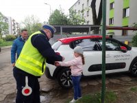 Policjant prowadzi zajęcia dla grupy przedszkolaków i rozdaje elementy odblaskowe