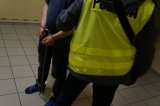 policjant w kamizelce odblaskowej i zatrzymany w kajdankach zespolonych