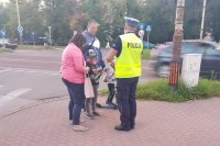 Policjant rozmawia z pieszymi i rozdaje odblaski