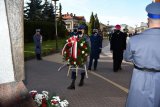 Policjant niosący wieniec, w tle delegacja służb mundurowych