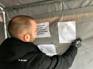 pracownik punktu sprzedaży wiesza wewnątrz ulotkę przygotowaną przez policjantów