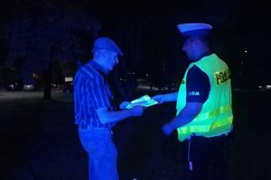 policjant wręcza kamizelkę mężczyźnie w świetle reflektora