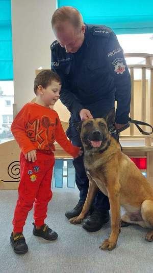 Zdjęcie przedstawia policjanta z psem służbowym. Obok stoi dziecko.