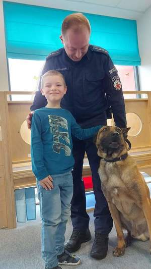 Zdjęcie przedstawia policjanta z psem służbowym oraz z dzieckiem.