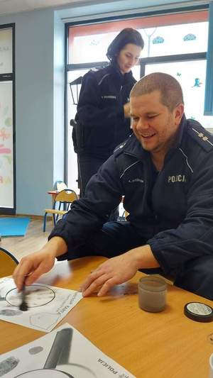 Zdjęcie przedstawia policjanta z kartą daktyloskopijną.