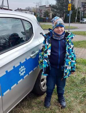 Zdjęcie przedstawia dziecko stojące przy radiowozie.