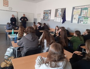 Zdjęcie przedstawia umundurowanych policjantów przemawiających do uczniów w sali lekcyjnej.