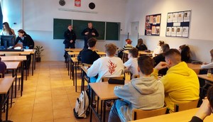 Zdjęcie przedstawia umundurowanych policjantów przemawiających do uczniów w sali lekcyjnej.