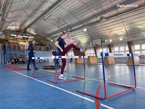 Zdjęcie przedstawia kobietę wykonującą ćwiczenia na torze przeszkód w sali gimnastycznej.