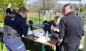 Zdjęcie przedstawia umundurowanych policjantów siedzących przy stole i znakujących przedmioty.