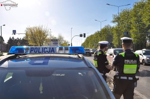 Zdjęcie przedstawia umundurowanych policjantów stojących obok radiowozu.