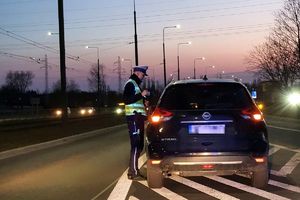 Zdjęcie przedstawia umundurowanego policjanta stojącego przy samochodzie.