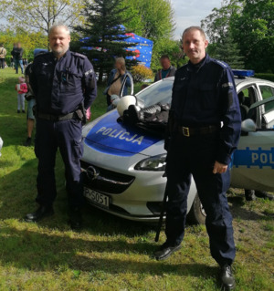 Zdjęcie przedstawia umundurowanych policjantów na tle radiowozu.