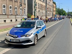 Zdjęcie przedstawia oznakowany radiowóz. W tle uczestnicy marszu.