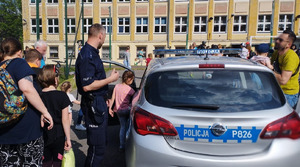 Zdjęcie przedstawia policjanta i nieoznakowany radiowóz. W tle dziecko wchodzące do radiowozu.
