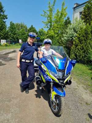 Zdjęcie przedstawia umundurowaną policjantkę stojącą obok motocyklu.