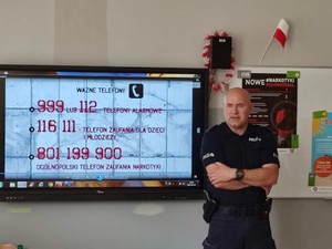 Zdjęcie przedstawia umundurowanego policjanta przemawiającego do uczniów.