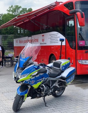 Zdjęcie przedstawia policyjny motocykl na tle autokaru z napisem &amp;amp;quot;Mobilny punkt poboru krwi&amp;amp;quot;.