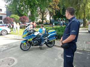 Zdjęcie przedstawia umundurowanego policjanta. W tle dzieci przy motocyklu służbowym.