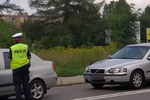 Zdjęcie przedstawia umundurowanego policjanta stojącego przy samochodach osobowych.