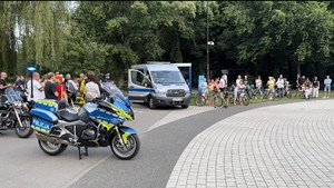 Zdjęcie przedstawia radiowóz służbowy i motocykl. W tle uczestnicy Festynu,