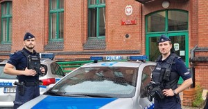 Zdjęcie przedstawia dwóch umundurowanych policjantów na tle radiowozu służbowego