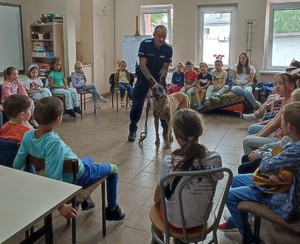 Zdjęcie przedstawia umundurowanego policjanta z psem służbowym oraz dzieci.