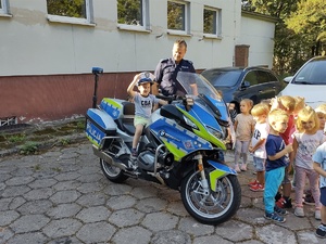 Zdjęcie przedstawia umundurowanego policjanta przy motocyklu służbowym wraz z dziećmi.