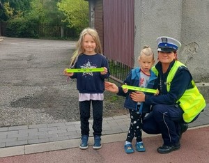 Zdjęcie przedstawia umundurowaną policjantkę oraz dzieci trzymające w rękach opaski odblaskowe.