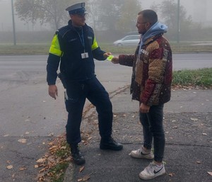 Zdjęcie przedstawia umundurowanego policjanta wręczającego mężczyźnie element odblaskowy.