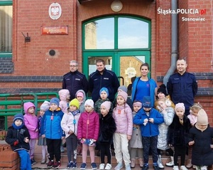 Zdjęcie przedstawia grupę dzieci oraz umundurowanych policjantów stojących przed wejściem do Komisariatu Policji II w Sosnowcu.