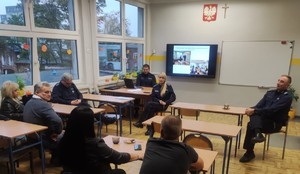 Zdjęcie przedstawia umundurowanych policjantów zwracających się do uczestników debaty. W tle prezentacja multimedialna.