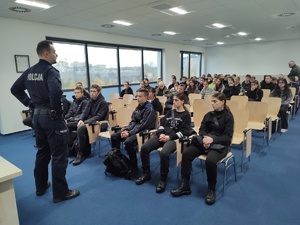 Zdjęcie przedstawia umundurowanego policjanta przemawiającego do uczniów.