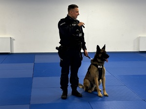 Zdjęcie przedstawia umundurowanego policjanta z psem służbowym.