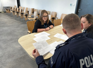 Zdjęcie przedstawia kobietę w okularach oraz umundurowanych policjantów.