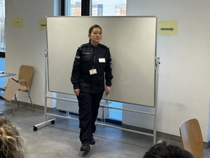 Zdjęcie przedstawia umundurowaną policjantkę przemawiającą do uczestników szkolenia.