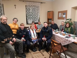 Zdjęcie przedstawia grupę seniorów i umundurowaną policjantkę na spotkaniu.