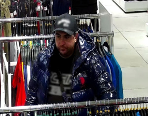 Zdjęcie przedstawia mężczyznę w czarnej czapce i ciemnej kurtce na terenie sklepu.