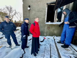 Zdjęcie przedstawia umundurowanych policjantów oraz księdza rozmawiających przed domem ze starszym mężczyzną.