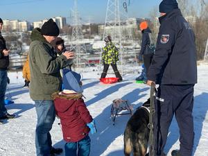Zdjęcie przedstawia umundurowanego policjanta z psem służbowym na stoku narciarskim.