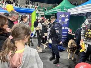 Zdjęcie przedstawia przewodnika psa służbowego z grupą ludzi przy stoisku.