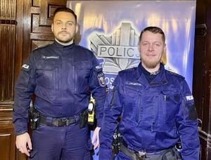 Zdjęcie przedstawia dwóch umundurowanych policjantów na tle napisu &quot;Policja&quot;.