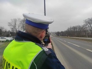 Zdjęcie przedstawia umundurowanego policjanta wydziału ruchu drogowego podczas służby w terenie.