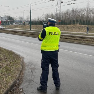 Zdjęcie przedstawia umundurowanego policjanta z wydziału ruchu drogowego mierzącego prędkość.