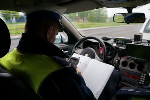 Zdjęcie przedstawia umundurowanego policjanta z wydziału ruchu drogowego w radiowozie służbowym.